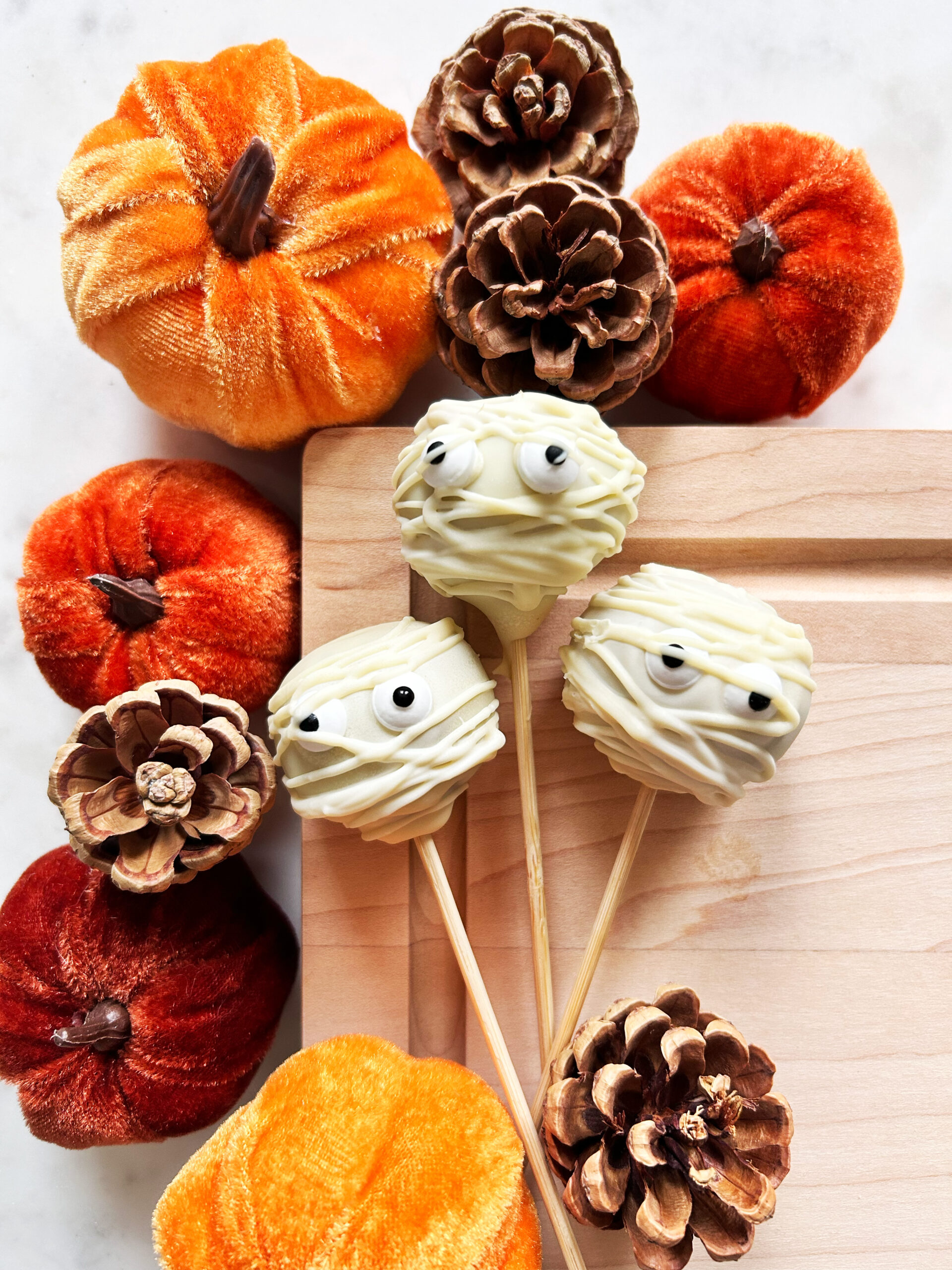 Cake pops deigned to look like mummies surrounded by miniature pumpkins and pinecones